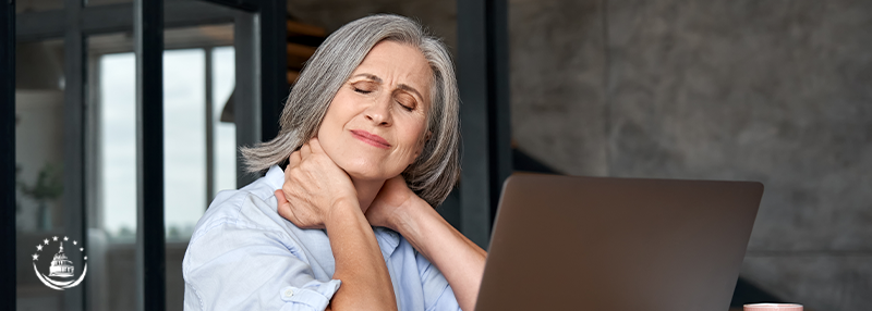 Woman clutching her neck with both hands with a look of pain on her face in front of a open laptop